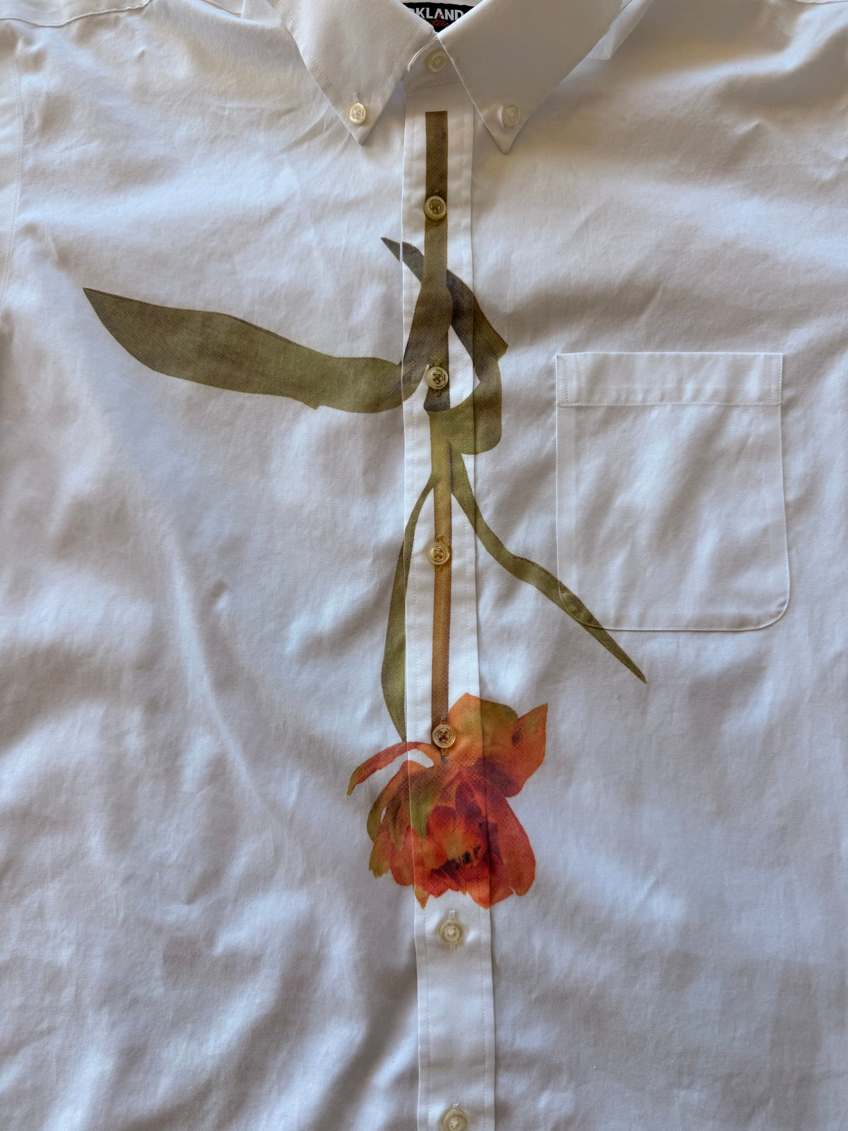 A white linen button-up shirt featuring a large, artistic print of a single orange-red tulip with green leaves and stem across the front.
