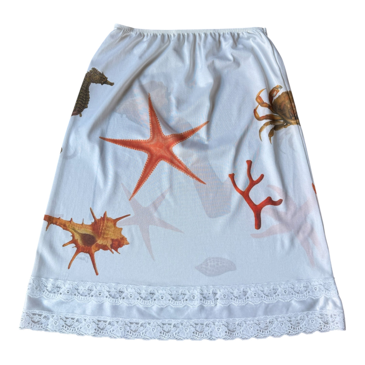 A white A-line skirt featuring an ocean-themed print with orange starfish, red coral, and brown seashells, finished with a white lace hem.