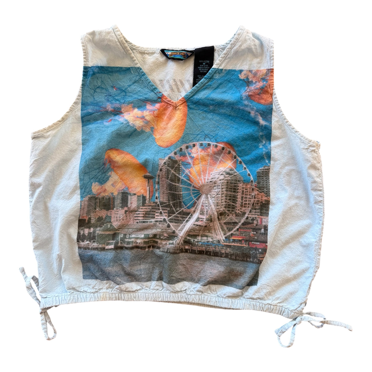 A sleeveless white crop top vest featuring a large graphic print of the Seattle skyline, including the Ferris wheel and jellyfish against a blue sky, with drawstring ties at the hem.