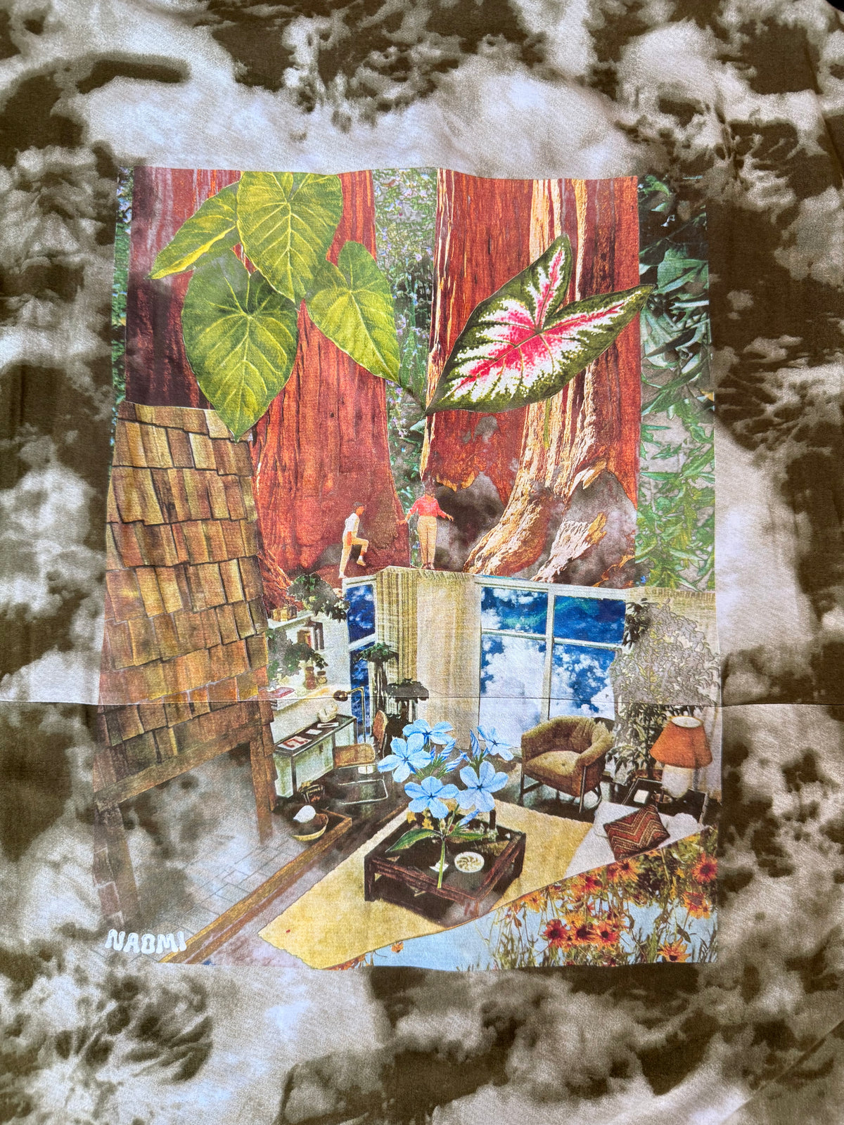 A square fabric print or patch featuring a surreal collage scene with giant redwood trees, large green and pink leaves, a small house, a chair, flowers, and blue sky, placed on a mottled gray, white, and brown background.