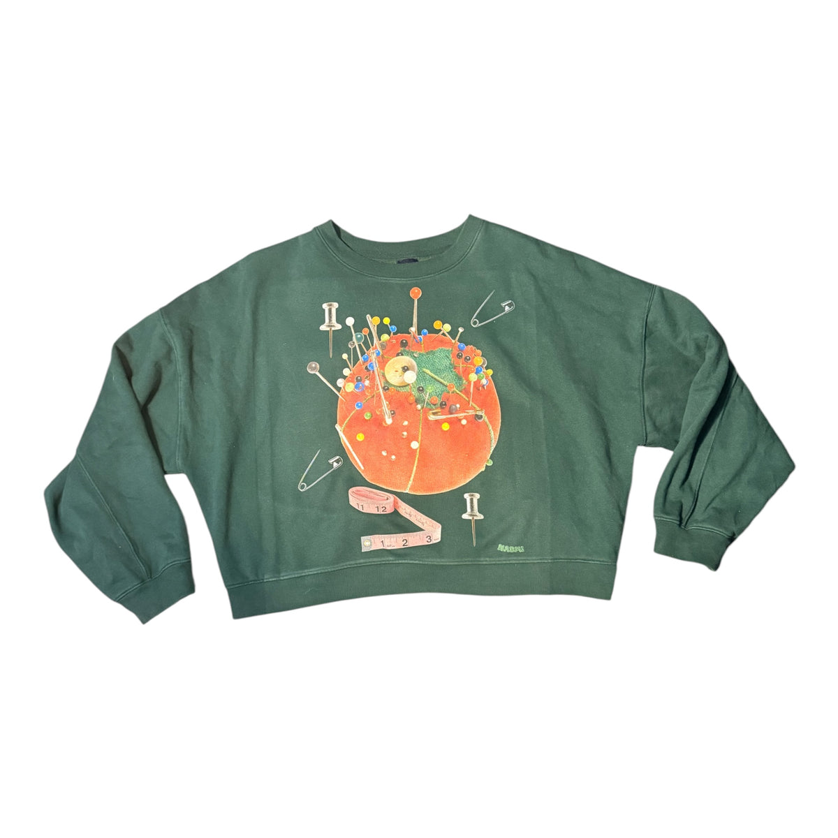A dark green crewneck sweatshirt featuring a colorful graphic of a pincushion with pins, safety pins, and a measuring tape on a white background.