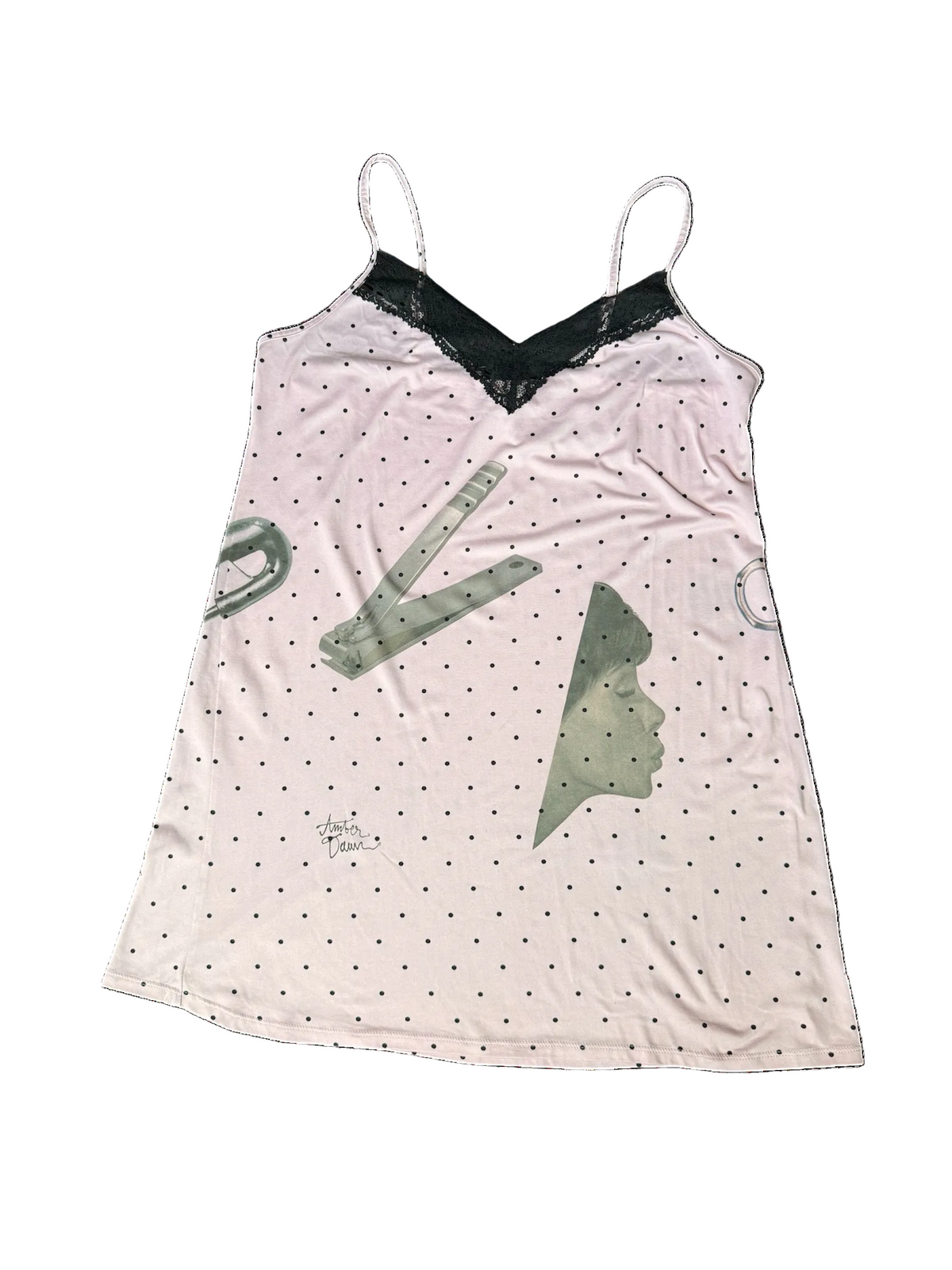 A light pink camisole nightshirt with black polka dots, a black lace V-neckline, and gray graphic illustrations of nail clippers, a safety pin and a profile silhouette.