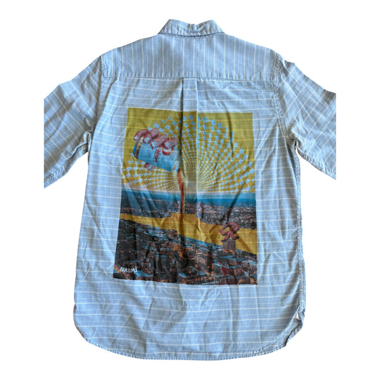 A light blue and white striped long-sleeve button-up shirt shown from the back, featuring a large colorful graphic print on the back with a hand holding a Rainier beer and a yellow geometric pattern.