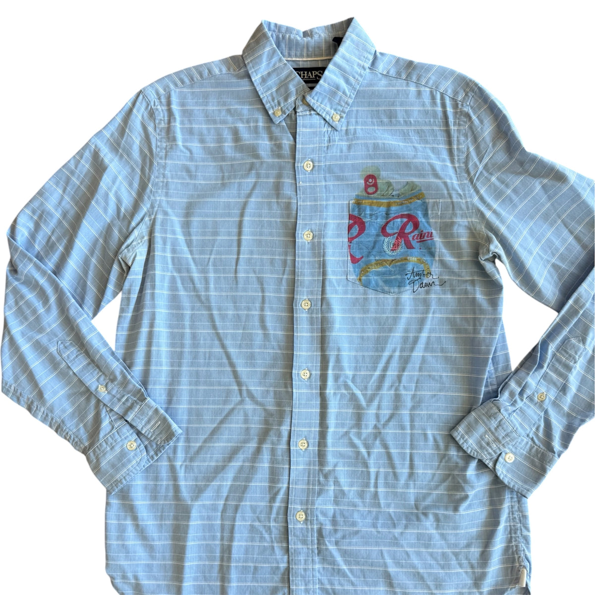 A light blue and white striped long-sleeve button-down shirt with a colorful Rainer beer graphic on the left chest, displayed flat against a white background.