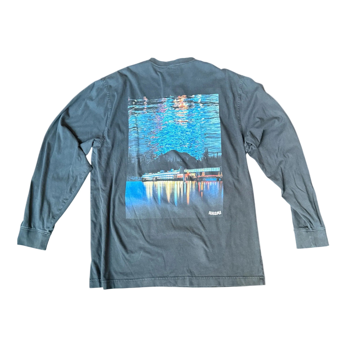 A long-sleeve t-shirt in a washed slate blue-gray color, shown from the back. It features a large rectangular graphic print depicting a scenic water reflection at night with a ferry and a bridge and mountains, and the brand name 'Naomi ' printed in white near the bottom right corner of the graphic.