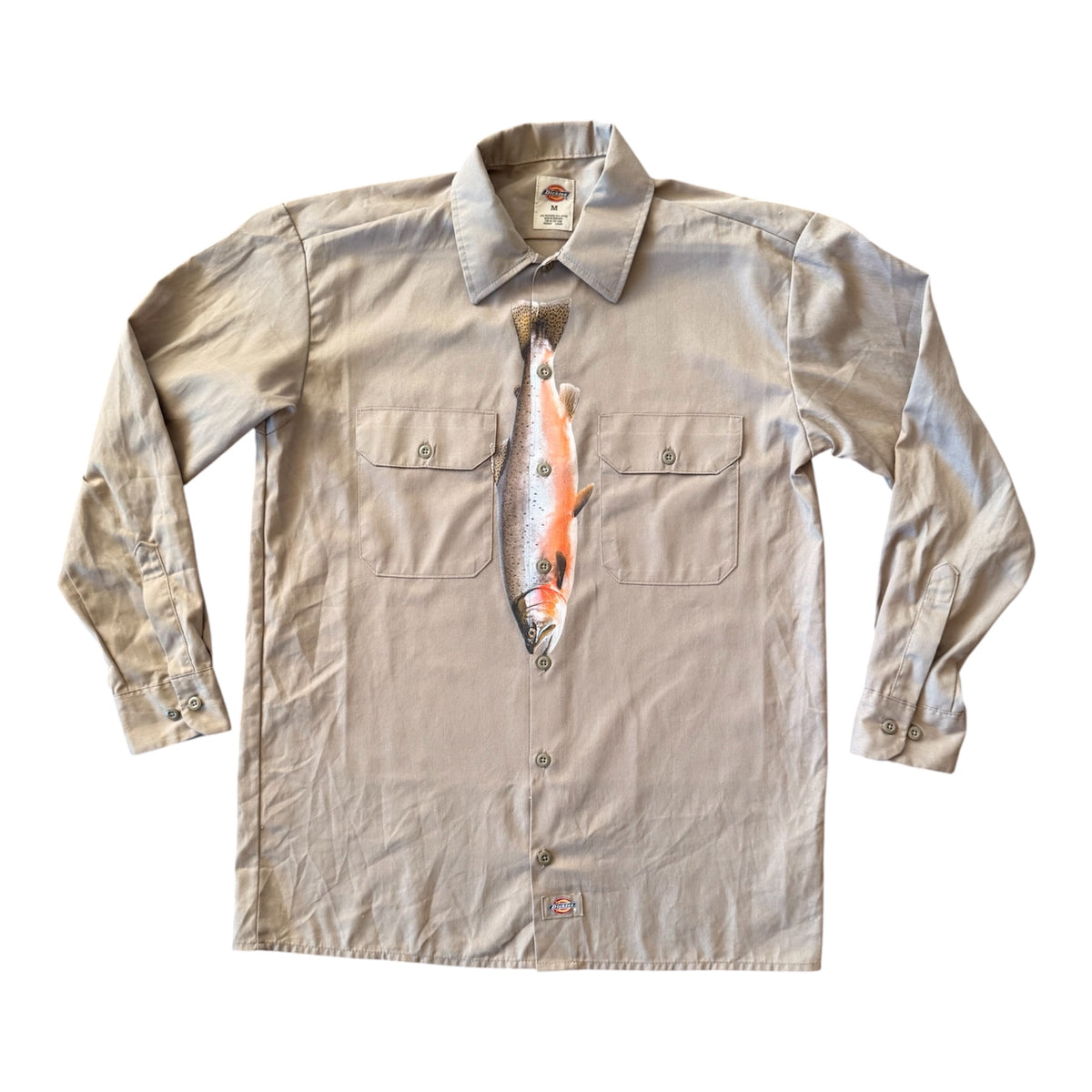 A light beige long-sleeve button-up shirt with a novelty fish-shaped chest pocket and a printed fish graphic on the front, displayed flat against a white background.