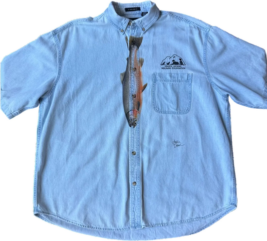 A light blue denim short-sleeve button-up shirt with a chest pocket and a printed fish graphic running vertically down the center front. The shirt features a ‘Shasta Animal Welfare Foundation' logo on the left chest.