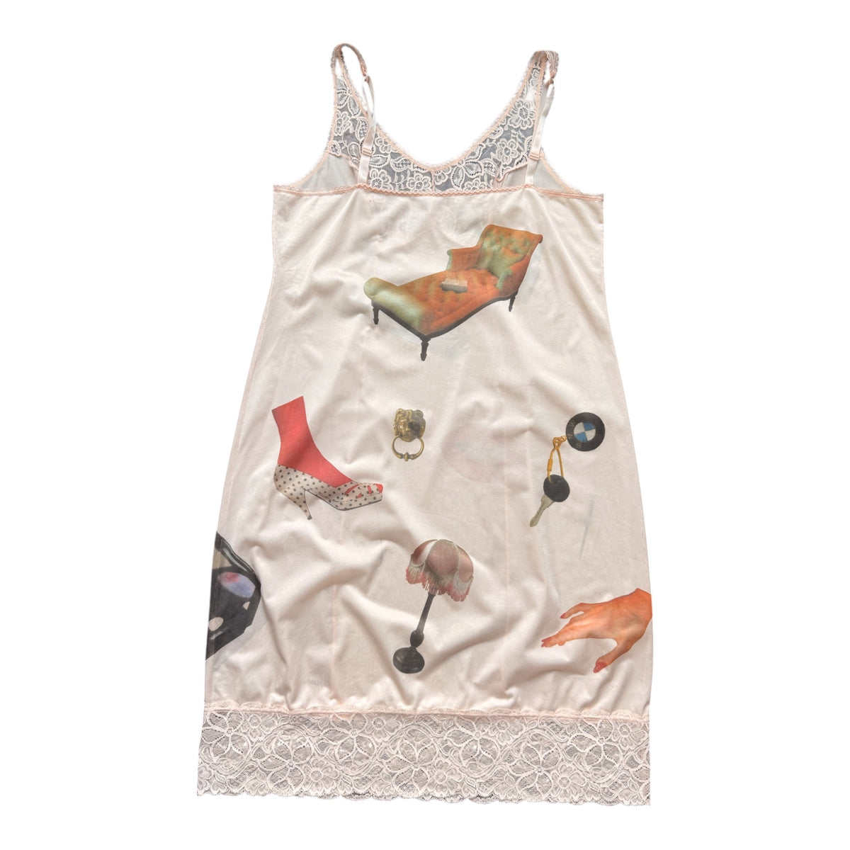 A light pink satin nightgown featuring a whimsical collage print of fashion and home items, including a red high-heeled shoe, a green chaise lounge, a handbag, a lamp, and a ring. The garment has lace trim at the neckline and hem and is displayed flat against a white background.