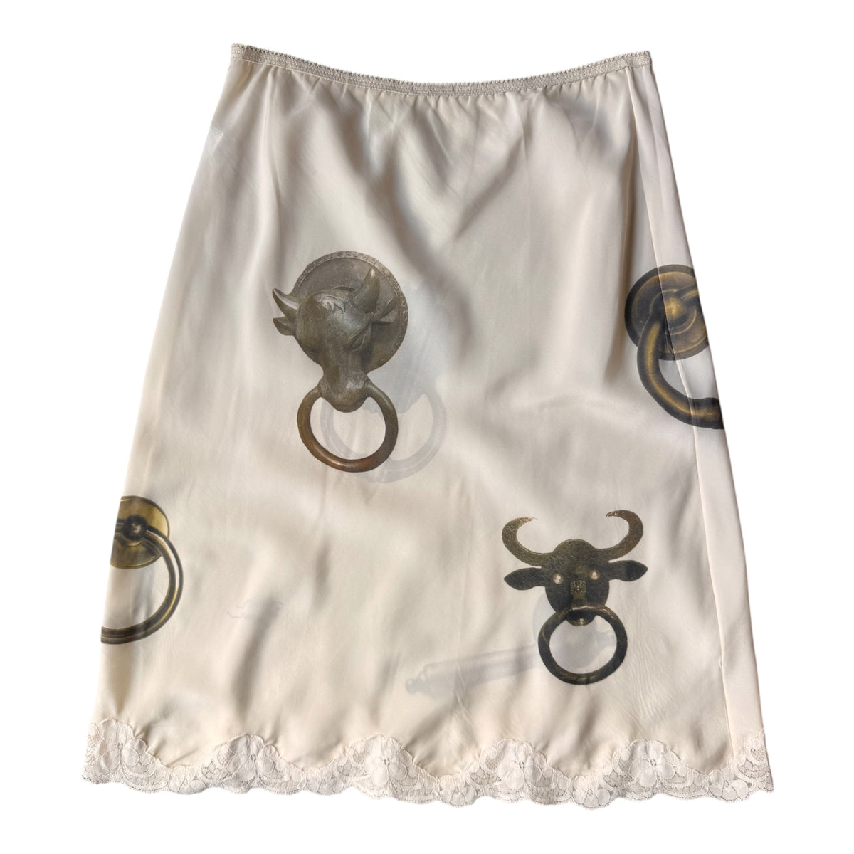 An off-white satin A-line skirt featuring a print of antique-style brass and bronze bull head door knobs with ring pulls, finished with a white lace hem.