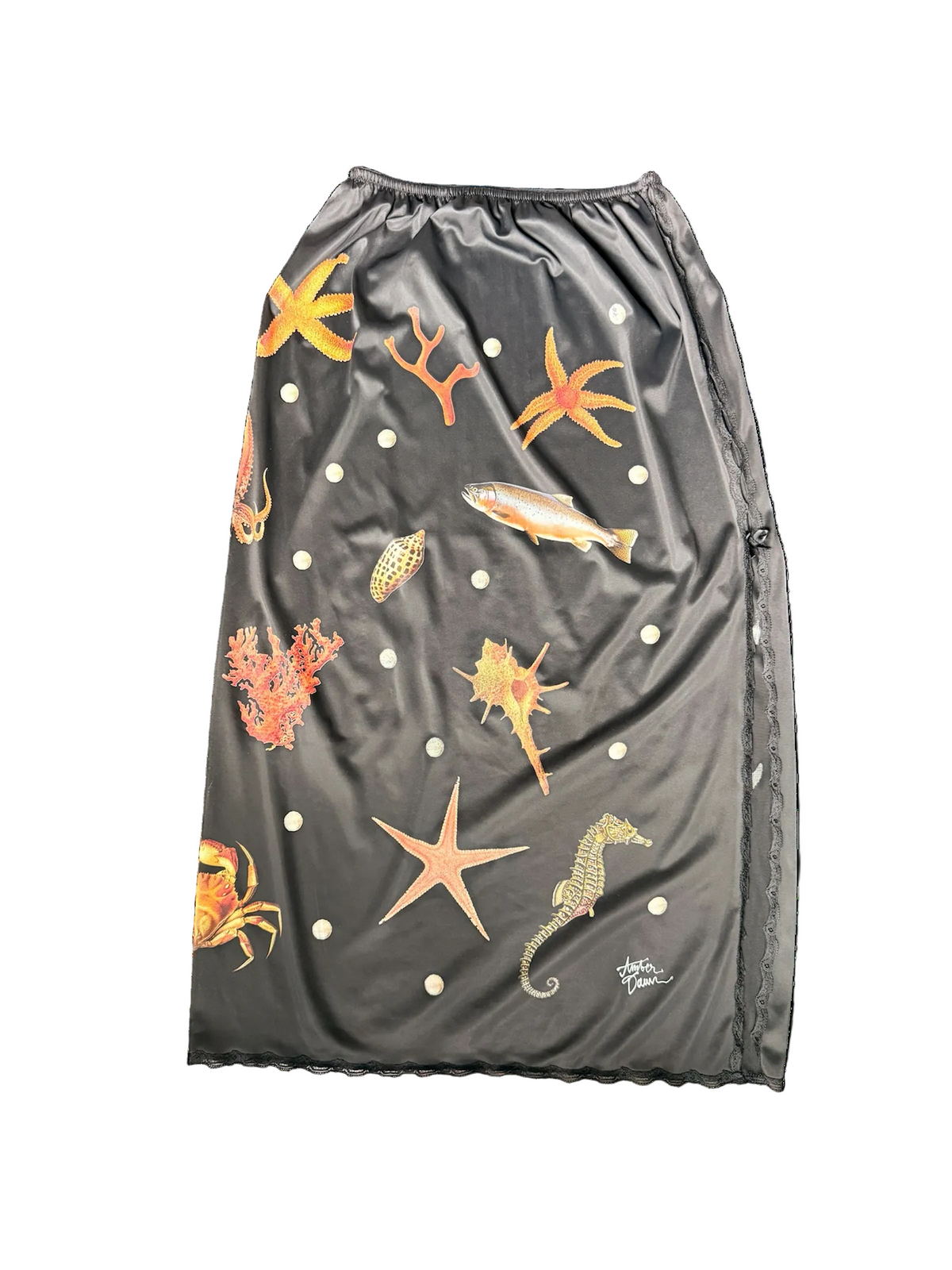 A black satin-like skirt featuring an all-over ocean-themed print with orange starfish, coral, a seahorse, a fish, and white polka dots, finished with a scalloped lace hem.