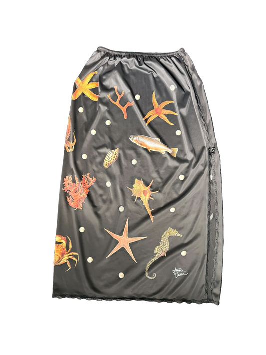 A black satin-like skirt featuring an all-over ocean-themed print with orange starfish, coral, a seahorse, a fish, and white polka dots, finished with a scalloped lace hem.