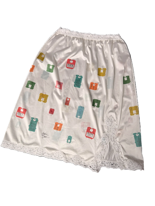 White satin nightgown with a colorful print of small bread clip icons and lace trim at the waistband and hem.