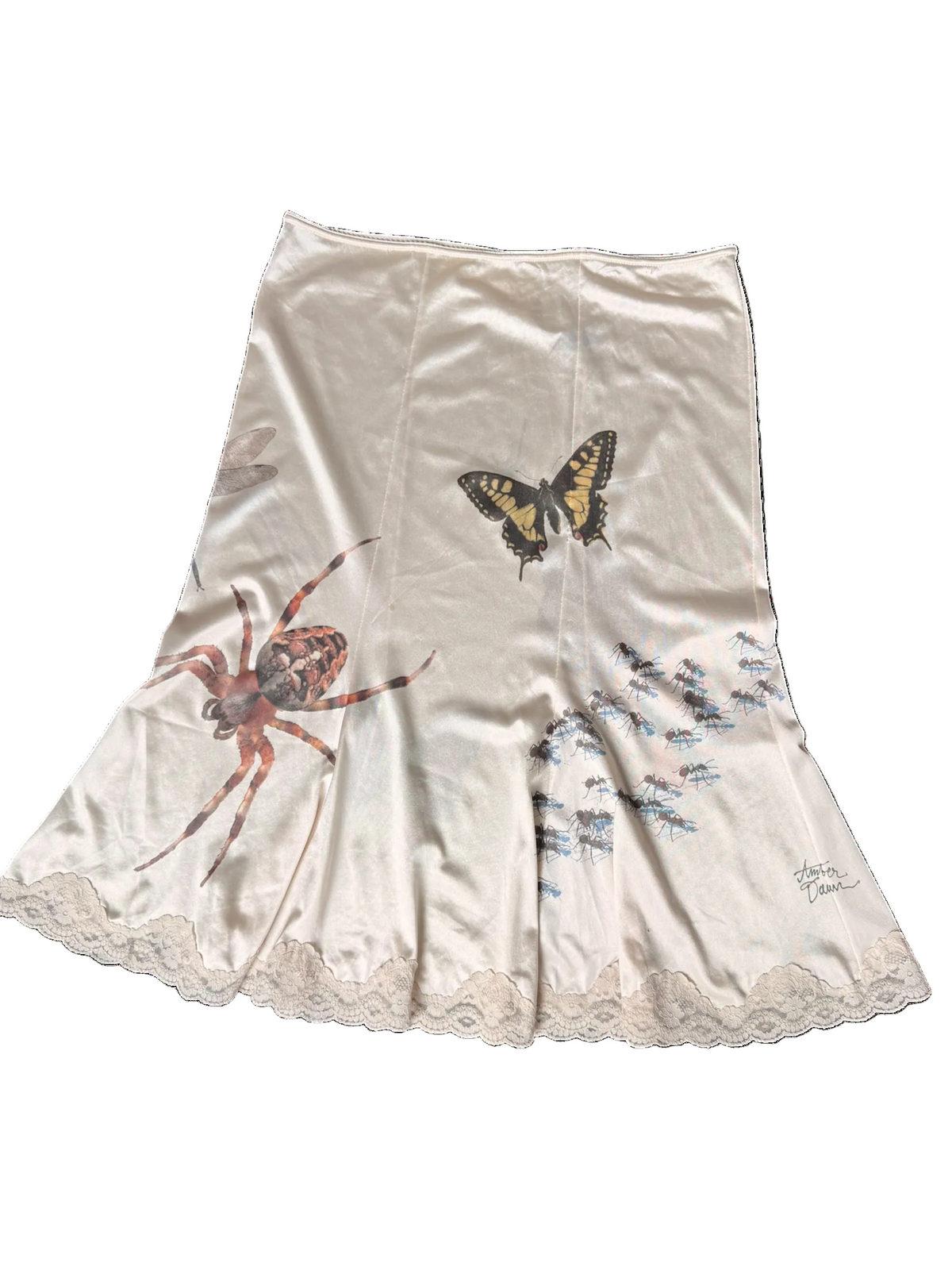 An off-white satin skirt featuring printed illustrations of a spider, a butterfly, and delicate ants, finished with a lace hem.