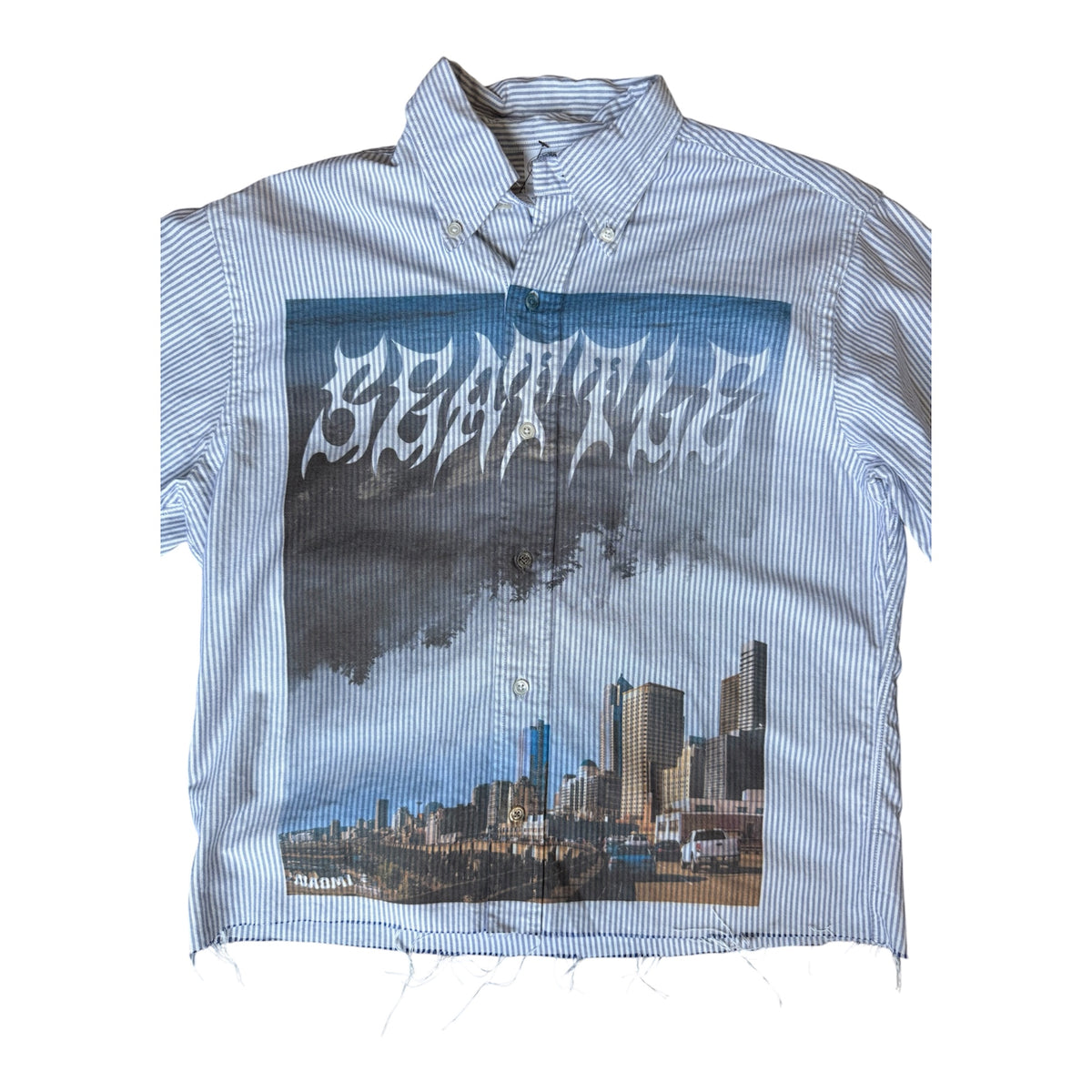 A short-sleeve button-down shirt with a blue and white stripe pattern, featuring a large front graphic print of the Seattle skyline with the word 'SEATTLE' in a stylized font.