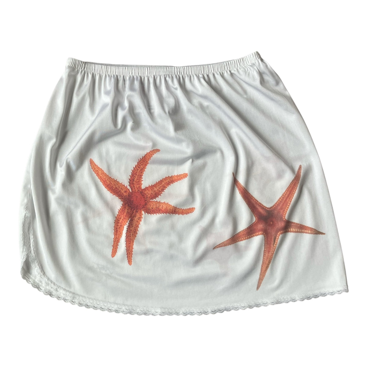 White skirt with two orange starfish prints, featuring an elastic waistband and a scalloped hem.