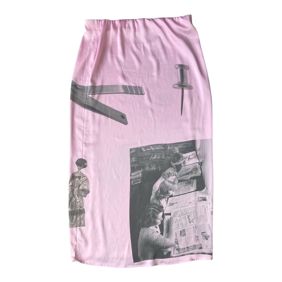 A light pink skirt featuring a collage print with black and white images of a woman reading a newspaper, a pushpin, and a ruler.