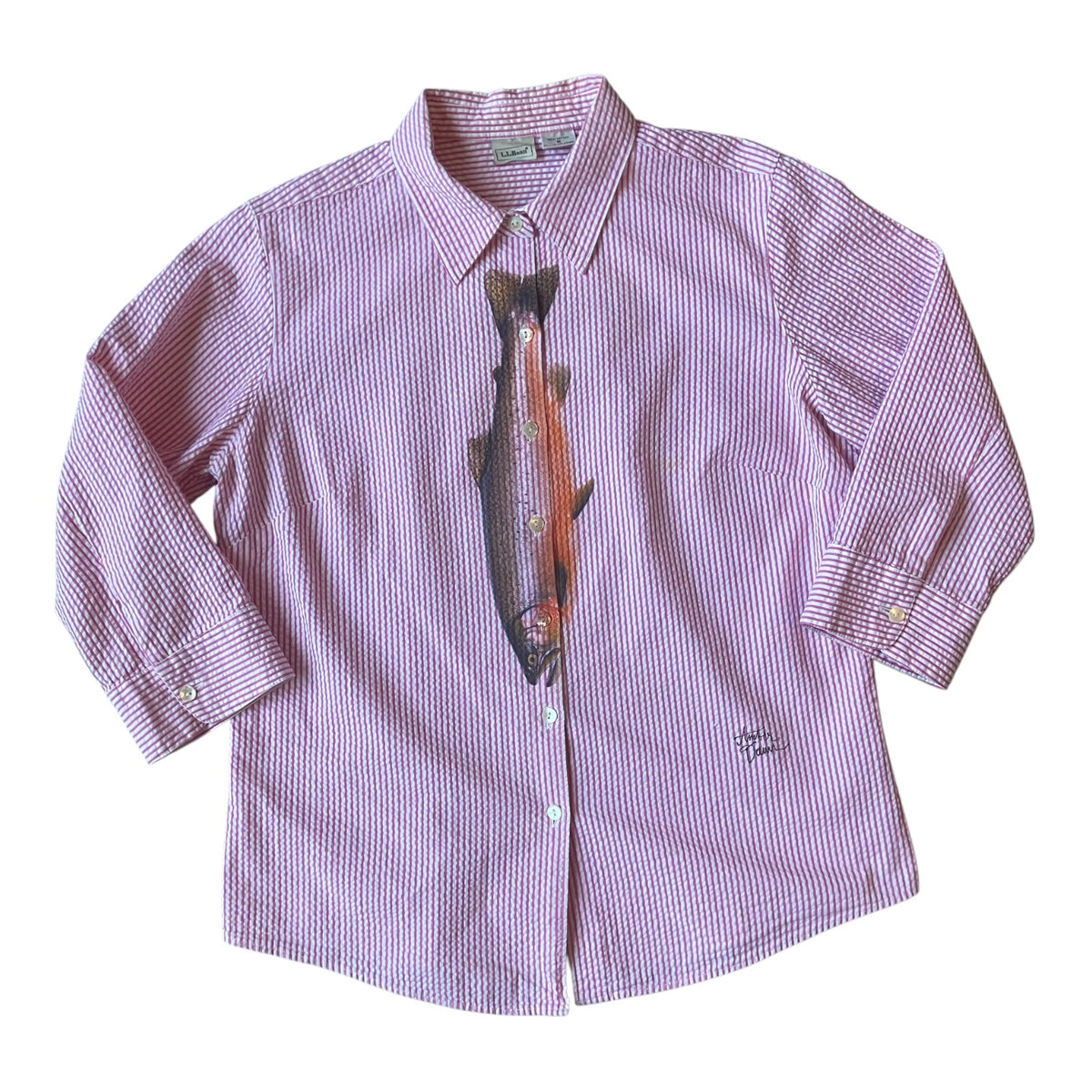 A pink and white striped long-sleeve button-down shirt featuring a large embroidered trout graphic on the front, displayed flat against a white background.