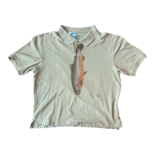 A short-sleeve polo shirt in a light beige green or sand color, featuring a large graphic print of a fish on the front. The shirt is laid flat against a solid white background.