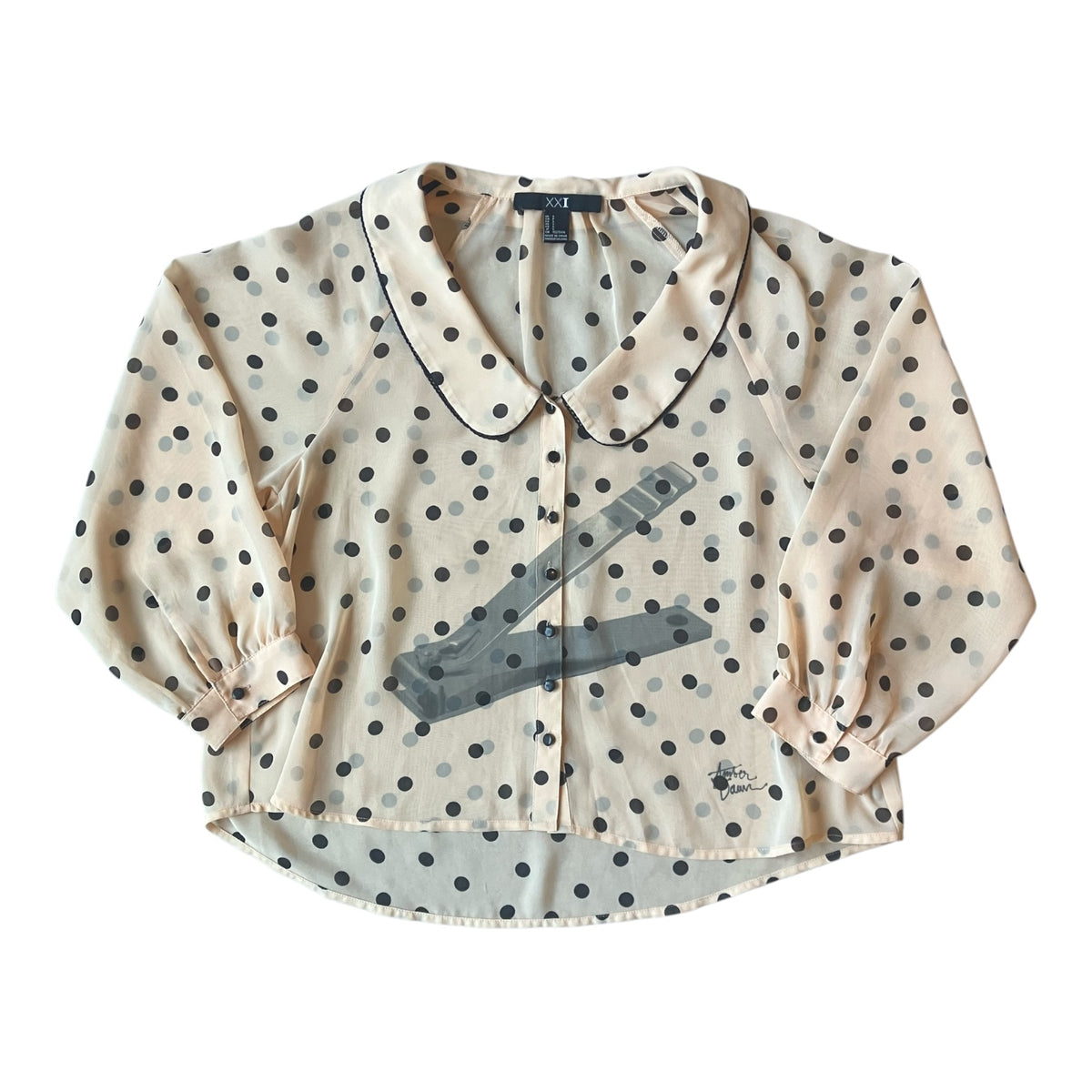 A cropped long-sleeve blouse with a cream base, black polka dots, and a gray graphic print of a nail clipper across the front, displayed flat against a white background.