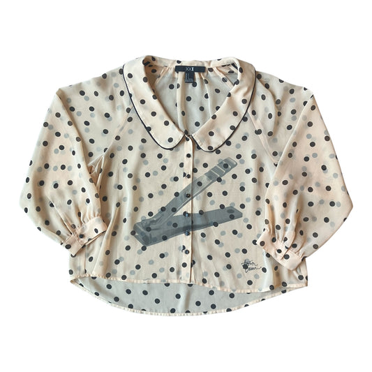 A cropped long-sleeve blouse with a cream base, black polka dots, and a gray graphic print of a nail clipper across the front, displayed flat against a white background.