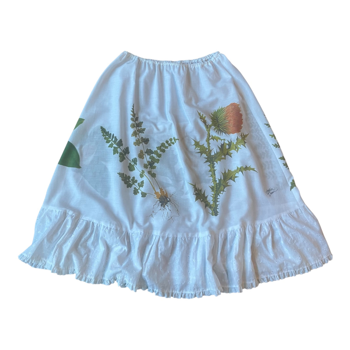 A white ruffled skirt featuring a botanical print of green ferns and a brown thistle, laid flat against a white background.