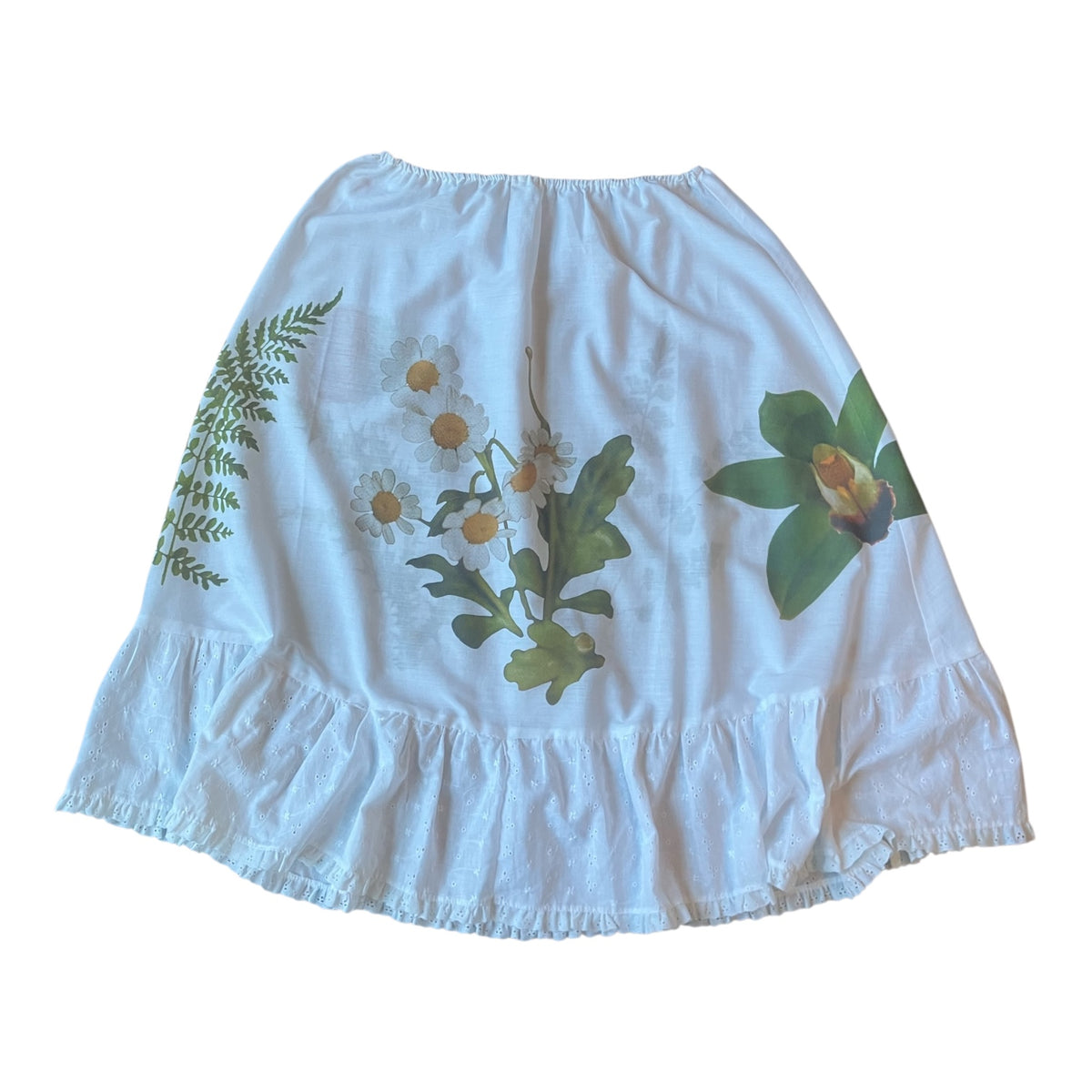 A white tiered skirt with a ruffled hem, featuring printed botanical illustrations of daisies, a fern, and a green orchid flower.